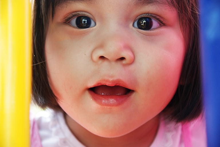 A young child looks intently at the camera with wonder between yellow and blur playground bars.